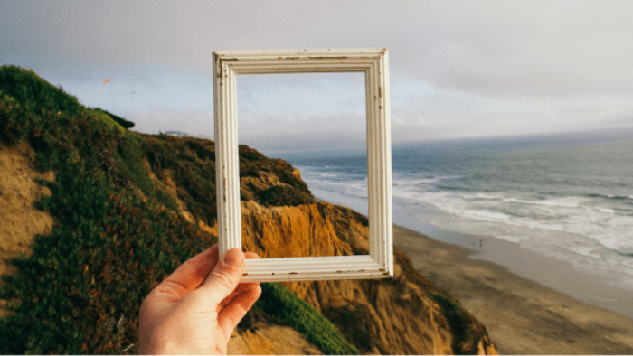 hand holding a frame looking at a coastal landscape